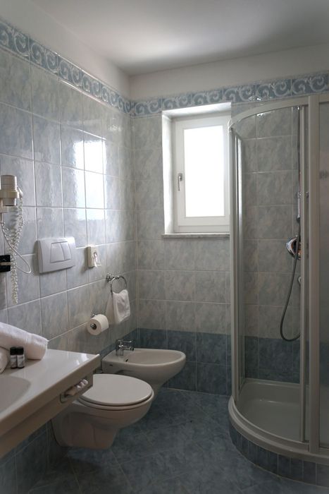 Ein hellblau gefliestes Badezimmer mit einer Duschkabine, einer Toilette, einem Bidet und einem Handwaschbecken.