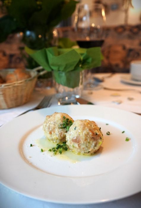 Zwei in Butter geschwenkte Semmelknödel garniert mit frischem Schnittlauch auf einem weißen Teller in einem Restaurant.