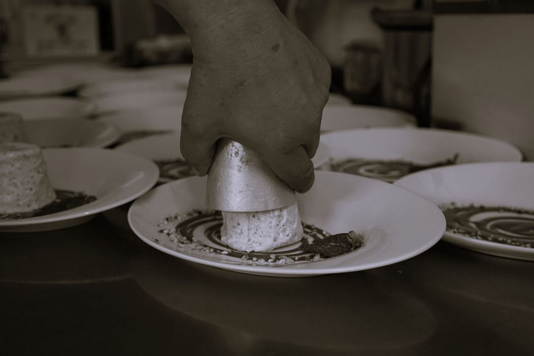 Eine Hand platziert eine zylindrische Form, um ein Dessert auf einem Teller in einer Küche anzurichten.