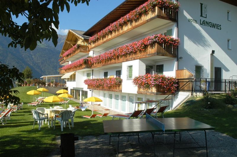 Hotel mit Blumenbalkonen, gelben Sonnenschirmen und Tischtennisplatte im Garten