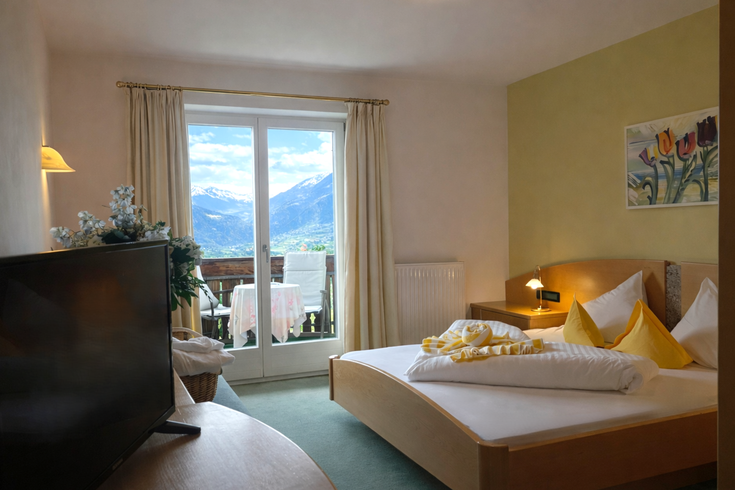 Innenansicht eines Hotelzimmers mit einem Doppelbett, einem Fernseher und einer Balkontür, durch die man eine Berglandschaft sieht.